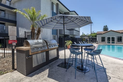 a barbecue and table with chairs in front of a swimming pool