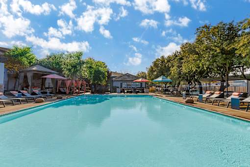A large swimming pool surrounded by trees and lounge chairs.