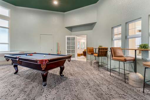A pool table is in the middle of a room with chairs around it.