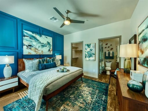 master bedroom with queen size bed and blue accent colored wall behind it. A door leads to the master bathroom and a second door shows the walk-in closet.at Craft at Gilbert and Baseline, Arizona  