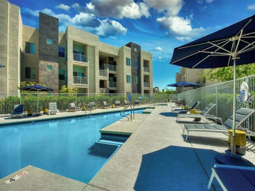 Pool with buildings in the background and patio umbrella up front. Four lounge chairs line the pool.at Craft at Gilbert and Baseline, Mesa, AZ 85204  