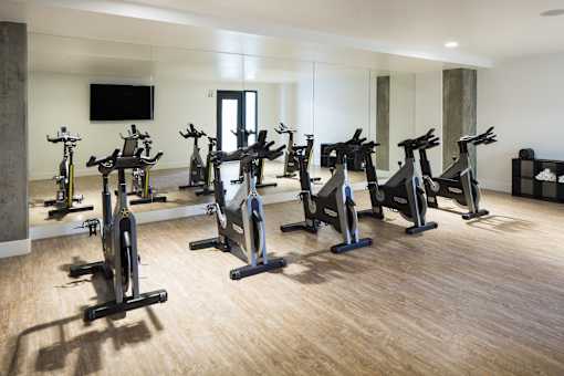 A room with a row of stationary bikes and a television mounted on the wall.