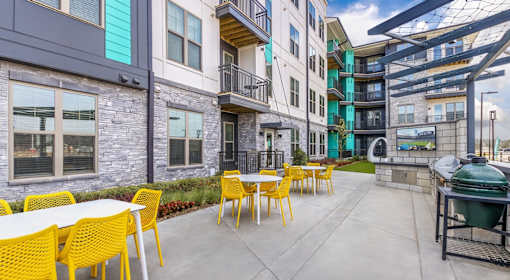 A patio with yellow chairs and tables is surrounded by apartment buildings.