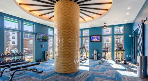 A gym with a blue carpet and a large yellow column in the middle.
