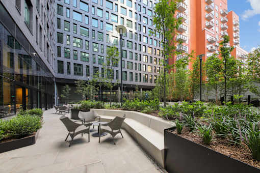 A patio with chairs and a bench is surrounded by plants and trees at Link Apartments® QPN, Long Island City, New York