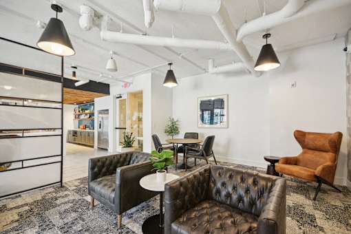a living room with leather couches and chairs and a kitchen at Link Apartments® 4th Street, Winston-Salem, NC, 27101