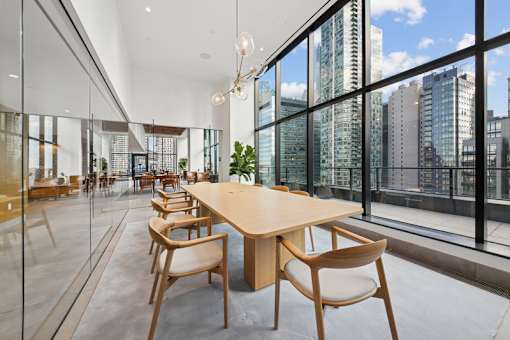 A conference room with a long table and chairs with a view of the city outside the windows at Link Apartments® QPN, Long Island City, New York
