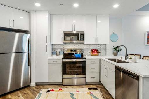 a white kitchen with stainless steel appliances and white cabinets at Link Apartments® Four 12, California