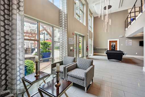 a lobby with chairs and a table in a building with large windows at Link Apartments® Brookstown, Winston Salem, NC, 27101