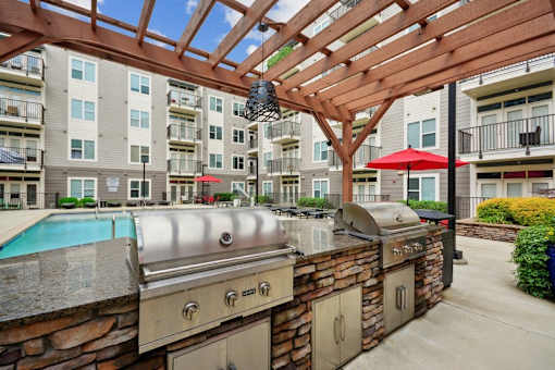 a patio with a grill and a pool with an apartment building at Link Apartments® Brookstown, Winston Salem, North Carolina