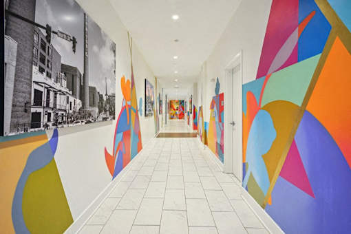 a hallway with colorful paintings on the walls and a white tile floor at Link Apartments® 4th Street, North Carolina, 27101