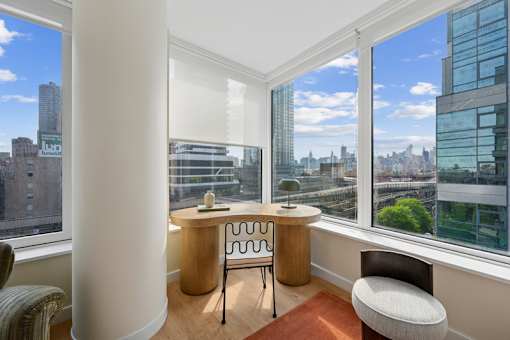 A room with a desk and chair in front of a window with a city view.at Link Apartments® QPN, New York