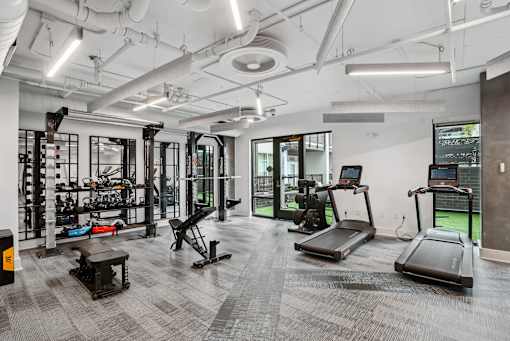 a workout room with treadmills and other equipment in a building with white walls at Link Apartments® Mint Street, Charlotte, NC