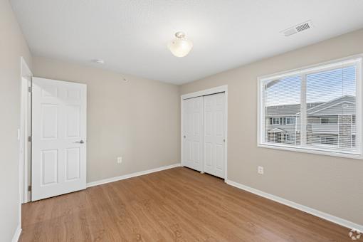 A room with a white door, a window with blinds, and a light on the ceiling.