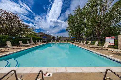 A swimming pool surrounded by lounge chairs and trees.
