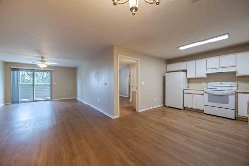 A spacious room with wooden floors and a kitchen area with white appliances.