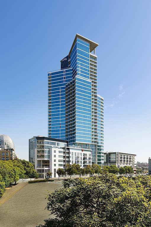 A tall blue building stands in front of a white dome and other buildings.