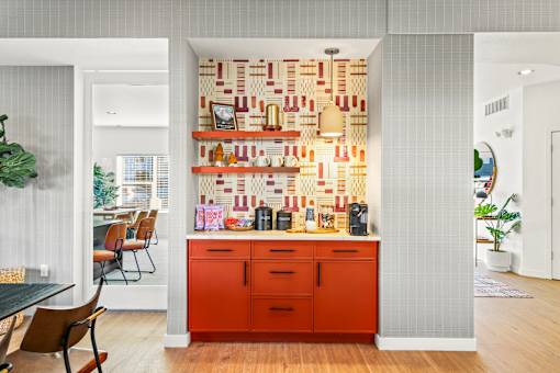 A kitchen with a red cabinet and a wall hanging with jars and bottles.