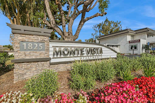 The sign for Monte Vista Apartments is surrounded by flowers and greenery.