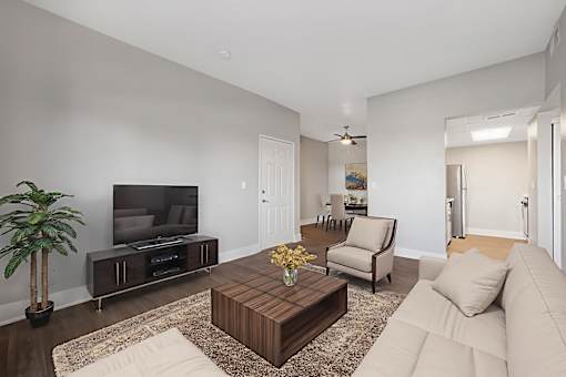A living room with a white couch, a wooden coffee table, a flat screen TV, and a potted plant.