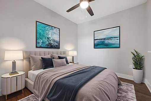 A bedroom with a bed, two lamps, a ceiling fan, and two pictures on the wall.