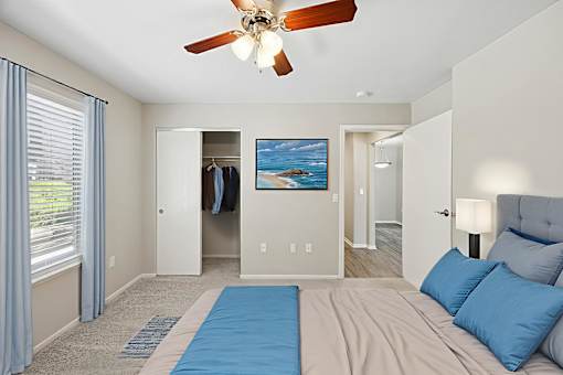 A bedroom with a bed, a ceiling fan, and a painting of a beach scene on the wall.
