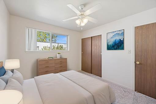 A bedroom with a large bed, a ceiling fan, and a painting on the wall.