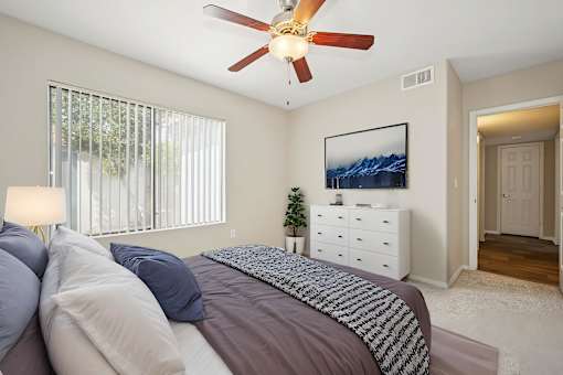A bedroom with a bed, a ceiling fan, and a painting on the wall.