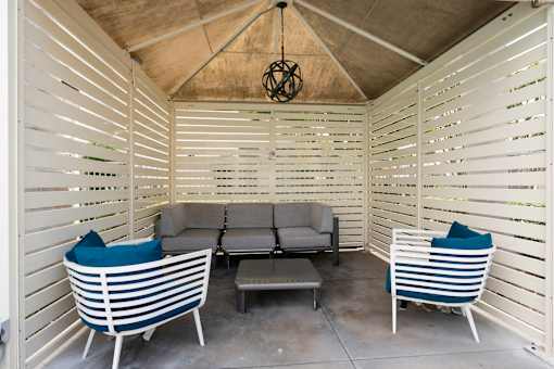 A white patio with a grey couch and two chairs.
