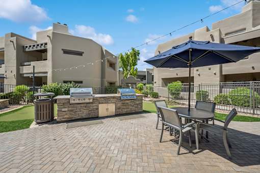 A patio with a table and chairs and a grill.