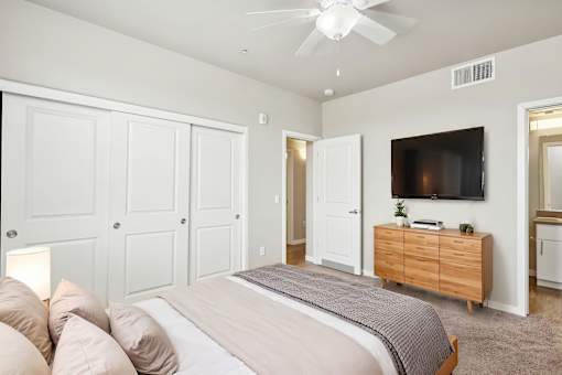 A bedroom with a large bed, a ceiling fan, and a TV mounted on the wall.