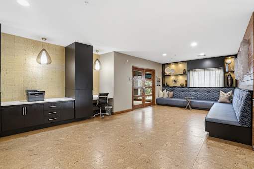 A spacious living room with a blue sofa and a kitchen area with a refrigerator.