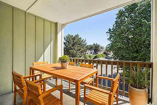 A wooden table and chairs on a balcony with a potted plant.