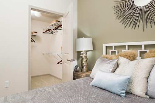 A bedroom with a bed, lamp, and a closet with clothes hanging.