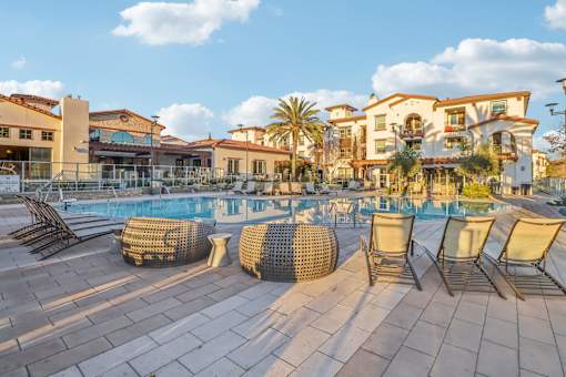 A pool surrounded by chairs and umbrellas with a building in the background.