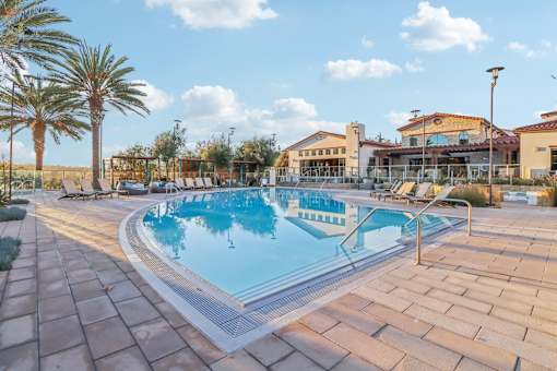 A large outdoor swimming pool surrounded by palm trees and a building in the background.