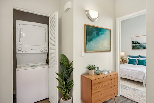 A small room with a white fridge, a wooden dresser, a potted plant, and a painting on the wall.