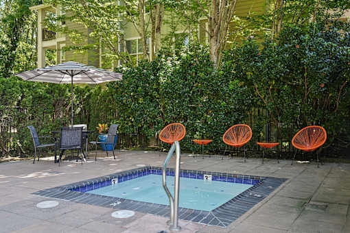 A pool surrounded by orange chairs and a green hedge.