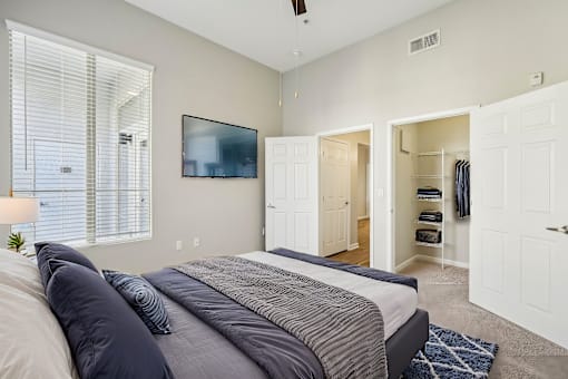 A bedroom with a bed, a window with blinds, a ceiling fan, and a closet with clothes.