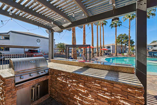 A patio with a grill and a pool in the background.