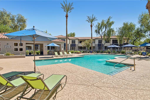 A pool surrounded by chairs and umbrellas with a building in the background.