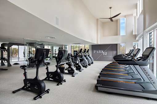 A gym with a row of treadmilers and elliptical machines.