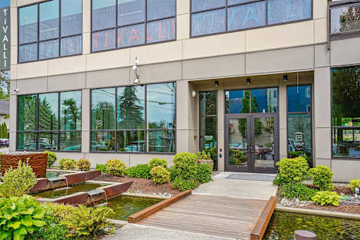 A modern building with a glass facade and a wooden walkway leading to the entrance.