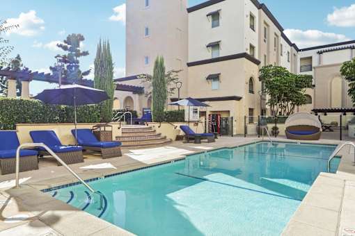 A pool surrounded by chairs and umbrellas in front of a building.