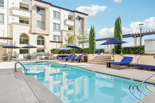 A swimming pool with blue loungers and umbrellas in front of a building.