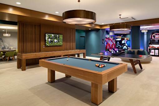 A pool table is in the middle of a room with a TV and a bar.