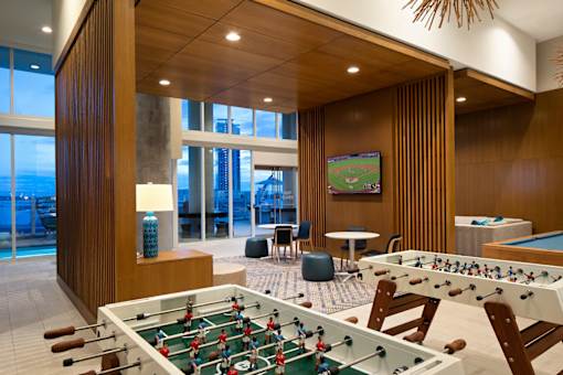 A foosball table is in the middle of a room with a pool table and a TV.