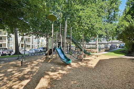 A playground with a green slide and a brown ground.