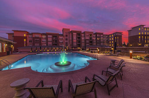 a pool with chairs and a fountain at night