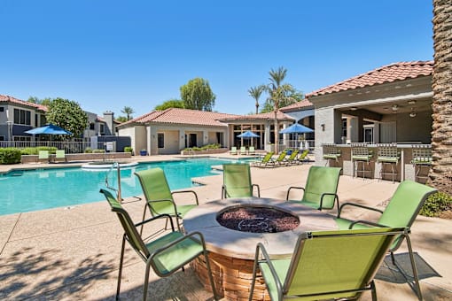 A poolside area with a fire pit and chairs.